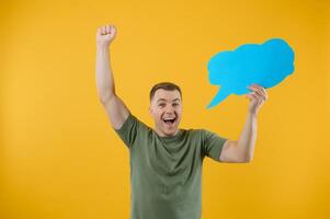 Cheerful young male pointing up and holding empty speech bubble with blank space for quote against vivid yellow background photo