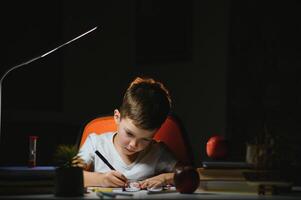 young teenager schoolboy at the table doing homework in the dark room photo