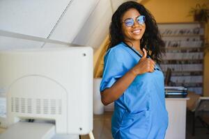 joven afro americano hembra médico en pie en clínica oficina cerca moderno ultrasonido máquina. foto