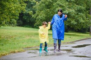 mamá y hijo en impermeables tener divertido juntos en el lluvia. concepto de familia vacaciones y contento infancia. foto