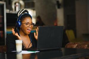 atractivo africano americano blogger con auriculares y ordenador portátil comunicado con seguidores en café foto