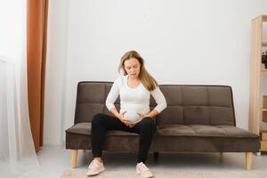 Pregnant woman getting up from sofa with hand on hip at home photo