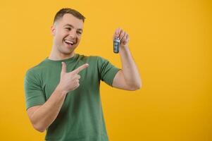 Happy smiling mature handsome european guy in t-shirt show finger at keys of new car, isolated on yellow background, free space. Success, victory, buy own first auto. Positive facial expression photo