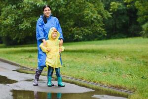 Mother with son walking in park in the rain wearing rubber boots photo