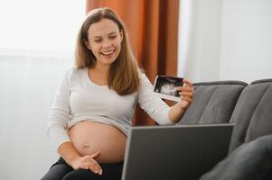 selective focus of happy pregnant woman showing ultrasound photos while having video call