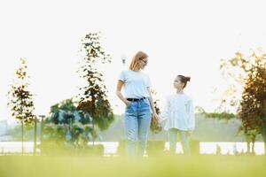 Attractive young woman with her little cute daughter are spending time together outdoors. Mom with daughter in park on a green grass during the sunset. photo