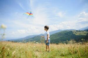 Little boy running on a background of mountains with kite. Sunny summer day. Happy childhood concept. photo