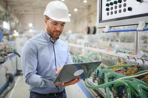 Engineer in hardhat is using a laptop in a heavy industry factory photo