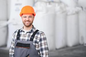 Portrait of man loader in uniform near big bag of coffee beans or wheat, nuts in warehouse of manufacturing factory photo