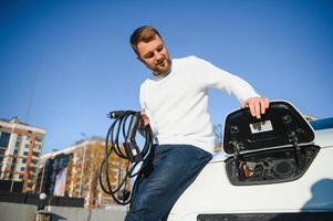 Man charges an electric car at the charging station photo