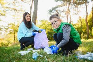 Smiling boy picking up trash in the park with his mother. Volunteer concept. photo