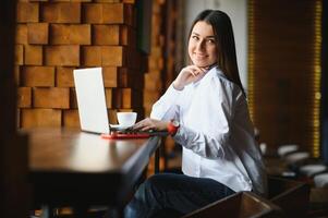 Beautiful Caucasian woman dreaming about something while sitting with portable net-book in modern cafe bar, young charming female freelancer thinking about new ideas during work on laptop computer photo