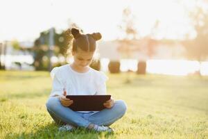 niño con tableta ordenador personal al aire libre. pequeño niña en césped con computadora foto