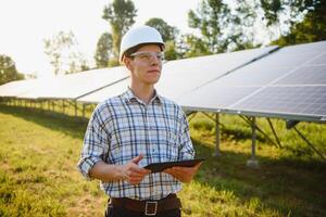 el retrato de un joven ingeniero cheques con tableta operación con sol, limpieza en campo de fotovoltaica solar paneles concepto renovable energía, tecnología, electricidad, servicio, verde fuerza. foto