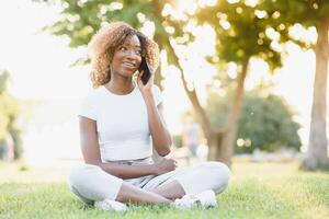 gente, tecnología y ocio concepto - contento africano americano joven mujer vocación en teléfono inteligente al aire libre foto