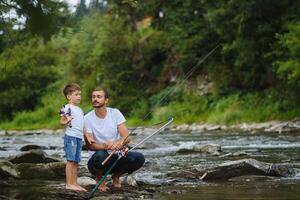 un padre enseñando su hijo cómo a pescado en un río fuera de en verano Brillo Solar foto