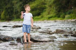 linda chico en blanco t camisa pescar en el río y tiene divertido, sonrisas vacaciones con niños, vacaciones, activo fines de semana concepto foto