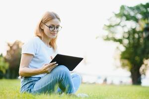 Young beautiful woman use mobile phone while sitting on the grass near the hotel, app, game, online shopping photo