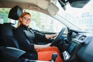 exitosa mujer de negocios conduciendo un automóvil a través de la ciudad urbana moderna con reflejos de edificios foto