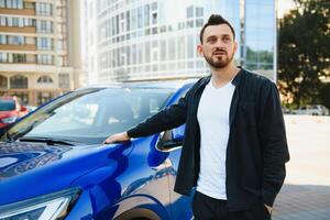 Portrait of a young man with a mobile phone in his hand near a car on a summer street. photo