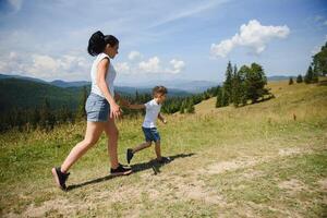 The boy and his mother are standing on the top of the mountain. A woman is traveling with child. Boy with his mother looking at the mountains. Travel with backpacks. Hike and climb with kids. photo