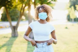 An outdoor portrait of a young African female with chestnut braids and in a virus protective mask on her face masked black woman outdoors with protection against influenza and pandemic threat photo