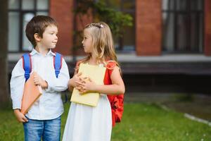 Happy children - boy and girl with books and backpacks on the first school day. Excited to be back to school after vacation. Full length outdoor portrait. photo