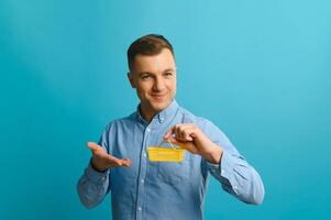 Young smiling man holding a mini shopping cart on a blue background. Sales concept. Place for text. photo