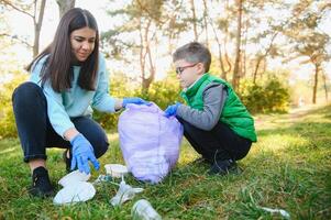 sonriente chico cosecha arriba basura en el parque con su madre. voluntario concepto. foto