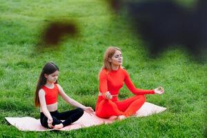 Mother and daughter doing yoga exercises on grass in the park at the day time photo