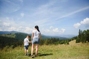 The boy and his mother are standing on the top of the mountain. A woman is traveling with child. Boy with his mother looking at the mountains. Travel with backpacks. Hike and climb with kids. photo