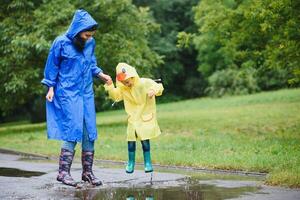 madre y niño, chico, jugando en el lluvia, vistiendo botas y impermeables foto