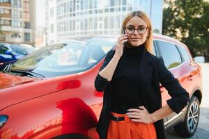 mujer utilizando móvil teléfono, comunicación o en línea solicitud, en pie cerca coche en ciudad calle o estacionamiento, al aire libre. coche intercambio, alquiler Servicio o Taxi aplicación foto