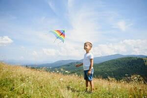 Little boy running on a background of mountains with kite. Sunny summer day. Happy childhood concept. photo