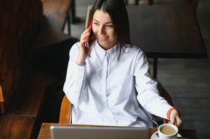 Young woman successful manager is talking via mobile phone with possible financial company employee and reading their resume on portable laptop computer during remote interview in co-working space photo