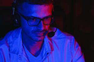 Pro Gamer. Millennial Guy Using Desktop Computer Playing Online Videogame Sitting At Night At Home. Neon Lights, Selective Focus photo