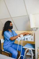 joven hembra afroamericano médico trabajando en moderno ultrasonido equipo. operador de ultrasonido exploración máquina sentado y mirando a el monitor, esperando para paciente. foto