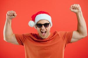 Portrait of happy and excited man in santa hat, rejoicing and winning something, celebrating new year, standing over red background photo
