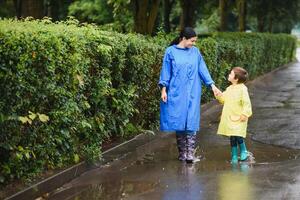 Mother and child, boy, playing in the rain, wearing boots and raincoats photo