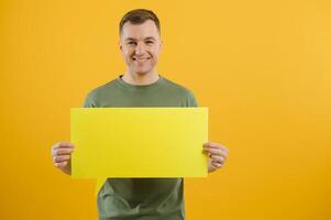 Happy guy smiling and holding blank speech balloon near head against yellow background photo