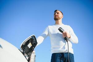 Stylish man inserts plug into the electric car charging socket photo