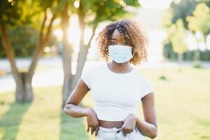 An outdoor portrait of a young African female with chestnut braids and in a virus protective mask on her face masked black woman outdoors with protection against influenza and pandemic threat photo