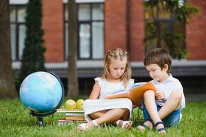 Schoolgirl sitting on green grass and talking to her friend they preparing for the lessons together before school photo