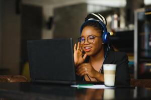 Attractive African American blogger with headphones and laptop communicating with followers in cafe photo