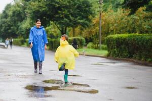 Mother with son walking in park in the rain wearing rubber boots photo