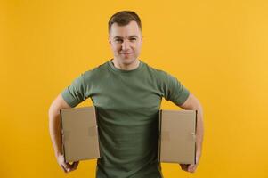 Delivery man in green uniform isolated on yellow background, studio portrait. Male employee working as courier dealer hold empty cardboard box. Service concept. Mock up copy space photo