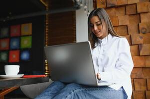 joven mujer exitoso gerente es hablando vía móvil teléfono con posible financiero empresa empleado y leyendo su currículum en portátil ordenador portátil computadora durante remoto entrevista en trabajo colaborativo espacio foto