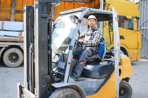 forklift driver in protective vest and forklift standing at warehouse of freight forwarding company, smiling photo