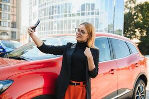 Woman using mobile phone, communication or online application, standing near car on city street or parking, outdoors. Car sharing, rental service or taxi app. photo