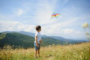 little boy holds string of kite flying in blue sky with clouds in summer with copyspace photo